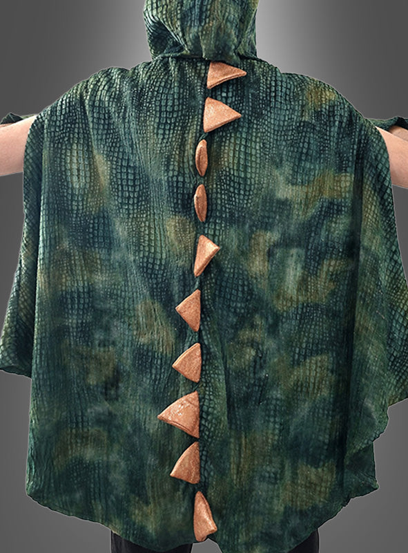 Eine Person, die einen grünen, strukturierten Umhang mit Kapuze trägt, an dessen Rücken orangefarbene dreieckige Stacheln entlanglaufen, ähnlich dem „Dino T-Rex Poncho für Erwachsene“.