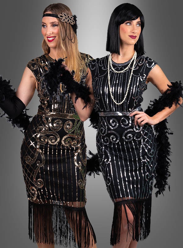 Zwei Frauen posieren elegant vor einem schlichten grauen Hintergrund und tragen jeweils umwerfende, von den 1920er Jahren inspirierte Flapper-Kleider – darunter das glamouröse „Premium 20er Jahre Kleider Kelly“, das mit Pailletten und Fransen verziert ist. Ergänzt durch Federboas und Stirnbänder fangen diese Charleston-Kleider den ikonischen Stil der 20er-Jahre-Kleider perfekt ein.