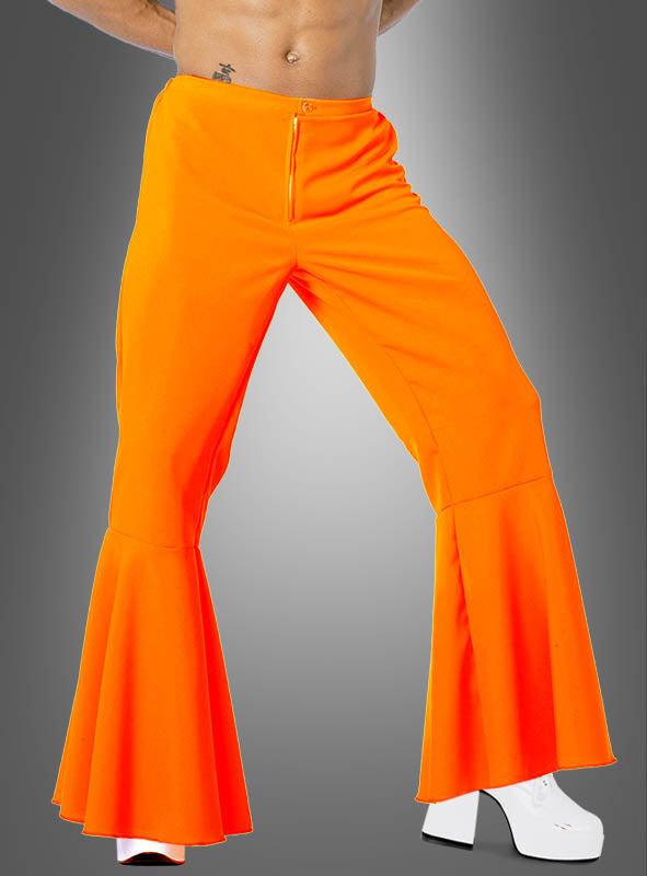 Eine Person in einer leuchtend orangefarbenen Neon-Schlaghose für Herren und weißen Plateauschuhen, die vor einem grauen Hintergrund mit Farbverlauf steht – das perfekte 70er-Jahre-Outfit.