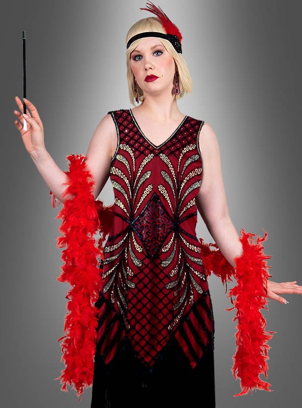 Eine Person trägt das „Exklusives 20er Flapper Kleid Vivian“ und ein mit Federn verziertes Stirnband. Sie steht anmutig da, eine Zigarettenspitze in der Hand und eine rote Federboa elegant über die Schultern drapiert, vor einem dezenten grauen Hintergrund mit Farbverlauf.
