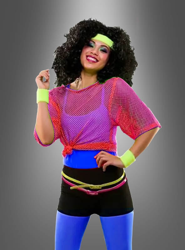Eine Person in knallbunter Sportkleidung im Stil der 1980er Jahre, darunter ein neonfarbenes Netzshirt im Stil der 80er Jahre, neonfarbene Damen-Leggings, ein Stirnband und Schweißbänder, die vor einem grauen Hintergrund steht und lächelt – perfekt für jedes 80er-Jahre-Party-Kostüm.