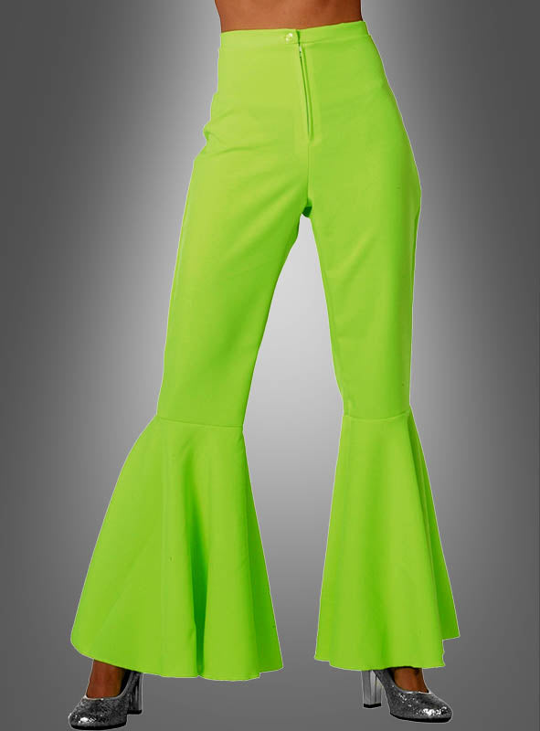 Eine Person, die eine leuchtend grüne Neon-Schlaghose „Damen Schlagerstar“ mit ausgestelltem Bein und silberne Stöckelschuhe trägt, wird von der Taille abwärts vor einem grauen Hintergrund mit Farbverlauf gezeigt.