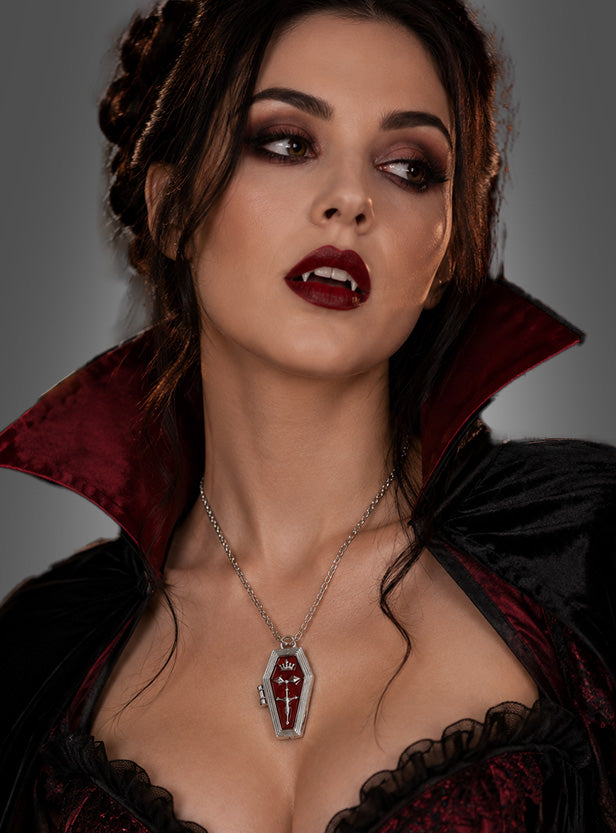 Eine Frau in einem Vampir-Kostüm mit auffälligem Make-up und einem dramatischen, schwarz-roten Umhang mit hohem Kragen präsentiert eine auffällige „Vampir-Kette mit Sarg-Anhänger“ – eine Halskette mit einem sargförmigen Anhänger, die perfekt für Halloween ist.