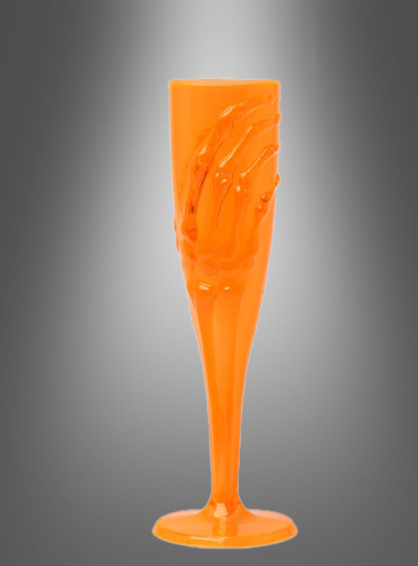 Das „Skeletthand Sektglas 20 cm“, ein orangefarbenes Sektglas aus Kunststoff mit einem Skeletthand-Motiv, wird vor einem schattierten grauen Hintergrund präsentiert – perfekt als Halloween-Tischdeko für Ihre nächste Gothic-Party oder gruselige Feier.