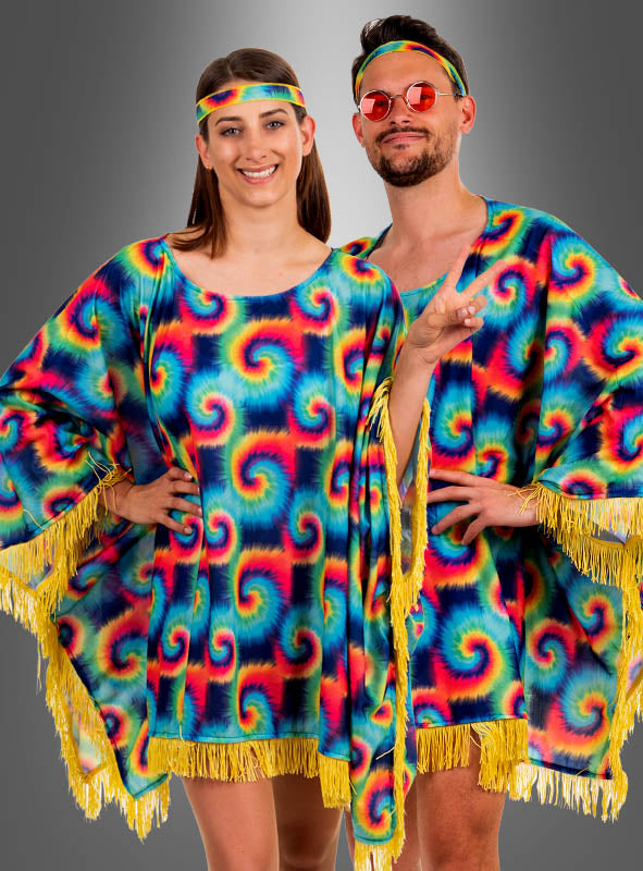Zwei Personen posieren in aufeinander abgestimmten, farbenfrohen Tie-Dye-Outfits, die den Geist eines echten 70er-Jahre-Kostüms perfekt einfangen. Eine Person trägt einen „Hippie-Poncho für Damen mit Batikmuster“, der mit verspielten gelben Fransen verziert ist, während ihre Begleiterin den lebhaften Batik-Look mit einer Sonnenbrille und einem Stirnband abrundet. Die Szene spielt sich vor einem schlichten grauen Hintergrund mit Farbverlauf ab.