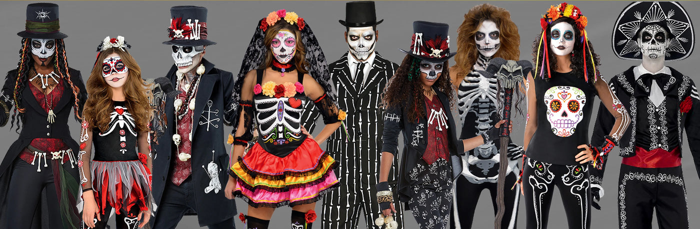 Eine Gruppe von Menschen trägt Kostüme zum Tag der Toten mit Gesichtsbemalung, Blumenkränzen und Outfits mit Skelettmotiven und steht nebeneinander.