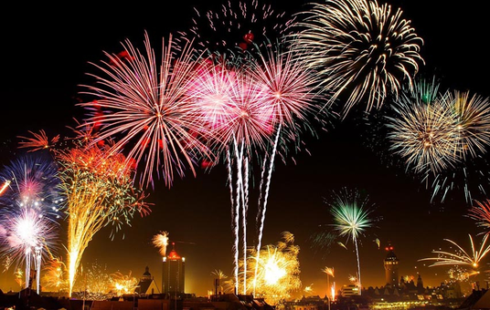 Bunte Feuerwerke explodieren am Nachthimmel über der Skyline einer Stadt, beleuchten die Gebäude und erzeugen lebhafte Lichtmuster.
