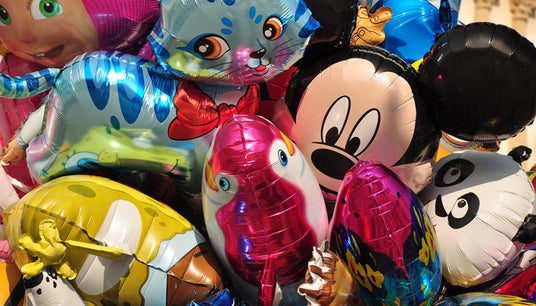Ein Bündel bunter, glänzender Heliumballons mit verschiedenen Tiergesichtern und Motiven von Zeichentrickfiguren.
