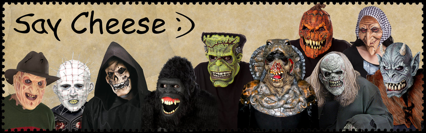 Eine Gruppe von Menschen, die verschiedene Monster- und Horrormasken tragen, posiert gemeinsam vor einem Schild mit der Aufschrift „Say Cheese :)“.