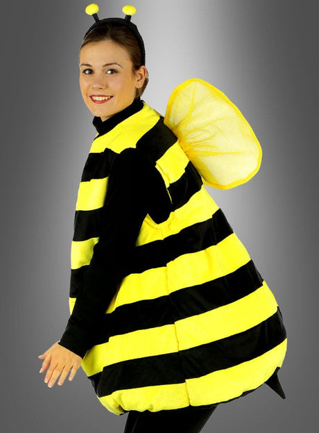 Eine Person, die ein Plüsch-Bienenkostüm für Erwachsene trägt – mit schwarzen und gelben Streifen sowie Flügeln und Fühlern –, steht vor einem grauen Hintergrund.