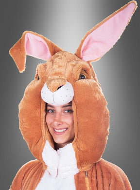 Eine Person, die lächelt, während sie das „Deluxe Hasenmaske Kopf Set waschbar“ trägt – ein braun-weißes Hasenkostüm mit großem Kopfteil, großen Ohren, rosa Futter und einem flauschigen Plüsch-Hasenkopf – vor einem grauen Hintergrund mit Farbverlauf.