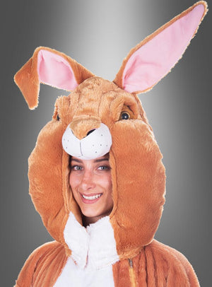 Eine Person, die lächelt, während sie das „Deluxe Hasenmaske Kopf Set waschbar“ trägt – ein braun-weißes Hasenkostüm mit großem Kopfteil, großen Ohren, rosa Futter und einem flauschigen Plüsch-Hasenkopf – vor einem grauen Hintergrund mit Farbverlauf.
