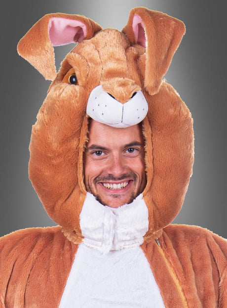 Vor einem grauen Hintergrund mit Farbverlauf trägt eine lächelnde Person das „Deluxe Hasenmaske Kopf Set waschbar“ – eine plüschige, braune Hasenmaske, die Kopf und Ohren bedeckt und an ein verspieltes Karnevalskostüm erinnert.