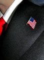 Nahaufnahme einer Person, die einen schwarzen Anzug, eine rote Krawatte und eine USA-Flaggen-Anstecknadel – eine elegante Anstecknadel mit der amerikanischen Flagge – am Revers trägt.