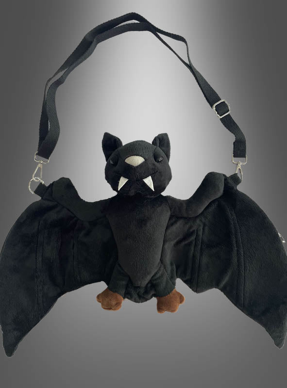 Die Fledermaus-Handtasche aus Plüsch mit schwarzen Flügeln, Stoffzähnen und braunen Füßen wird vor einem grau verlaufenden Hintergrund präsentiert – eine bezaubernde Plüsch-Umhängetasche und das perfekte Kostüm-Accessoire für jedes verspielte Outfit.
