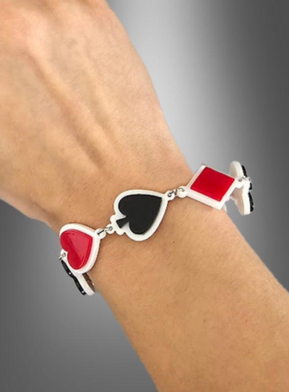 Ein silbernes Las-Vegas-Poker-Armband mit Anhängern in Form eines roten Herzens, eines schwarzen Pik-Symbols, eines roten Karos und eines schwarzen Kreuz-Symbols, das am Handgelenk einer Person vor einem grauen Farbverlaufs-Hintergrund getragen wird.
