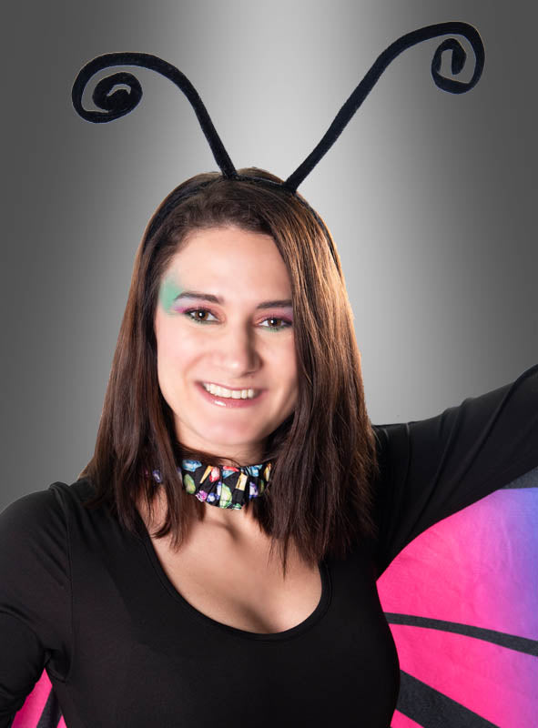 Eine Person in einem Schmetterlingskostüm, die den Haarreif „Schmetterling Fühler für Insekten verstellbar“ mit zarten, verstellbaren Fühlern sowie ein bunt gemustertes Halsband und leuchtend rosa und lila Schmetterlingsflügel trägt, steht vor einem grauen Hintergrund mit Farbverlauf.