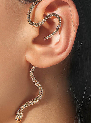 Ein goldener Schlangen-Ohrschmuck schlängelt sich elegant am äußeren Rand des Ohrs entlang, wobei der Kopf der Schlange unter dem Ohrläppchen hängt und sich ihr Schwanz über das Ohr krümmt – ein auffälliges Schmuckstück aus einer goldenen Modeschmuckkollektion, das jedem Look einen besonderen Akzent verleiht.