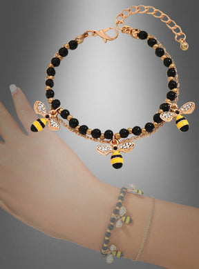 Der „Bienen Armband Kostümschmuck“ besteht aus einem goldenen Armband mit schwarzen Perlen und zwei Bienen-Anhängern, die Ihrem Look eine verspielte Note verleihen. Vor einem Farbverlaufshintergrund präsentiert und elegant am Handgelenk in Szene gesetzt, eignet sich dieses zarte Bettelarmband perfekt für jeden Anlass.