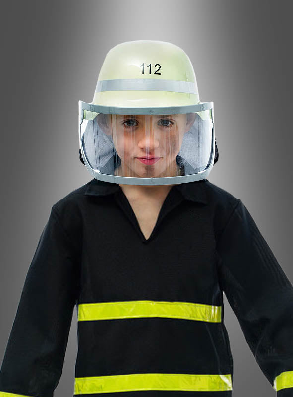 Ein Kind, das einen Feuerwehrhelm mit Visier und eine Uniform trägt und auf dessen Helm die Zahl 112 zu sehen ist, steht stolz vor einem schlichten grauen Hintergrund.