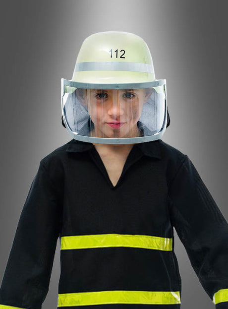 Ein Kind, das einen Feuerwehrhelm mit Visier und eine Uniform trägt und auf dessen Helm die Zahl 112 zu sehen ist, steht stolz vor einem schlichten grauen Hintergrund.