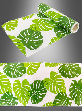 Eine Rolle „Bedruckter Palmblätter Tischläufer 3 Meter“ zeigt ein grünes Monstera-Blattmuster auf weißem Hintergrund, ideal als Hawaii-Tischläufer oder für die Partydekoration; abgebildet sowohl aufgerollt als auch in einer Nahaufnahme in flachem Zustand.