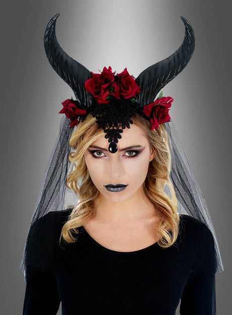 Eine Frau mit welligem blondem Haar trägt einen schwarzen Spitzenkopfschmuck und den gotischen Kopfschmuck mit langen Hörnern, Rosen und Schleier, der sich durch schwarze Hörner, rote Rosen, schwarzen Lippenstift und ein schwarzes, mit einem schwarzen Schleier drapiertes Outfit vor einem grauen Farbverlaufshintergrund auszeichnet.