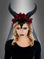 Eine Frau mit welligem blondem Haar trägt einen schwarzen Spitzenkopfschmuck und den gotischen Kopfschmuck mit langen Hörnern, Rosen und Schleier, der sich durch schwarze Hörner, rote Rosen, schwarzen Lippenstift und ein schwarzes, mit einem schwarzen Schleier drapiertes Outfit vor einem grauen Farbverlaufshintergrund auszeichnet.