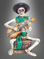 Skelettfigur „Mexikaner mit Gitarre“, 15 cm – eine Skelettfigur mit schwarzem Hut und grünem Schal, die auf einer Kiste sitzt und vor einem grauen Hintergrund mit Farbverlauf Akustikgitarre spielt. Perfekt als einzigartige „Day of the Dead“-Figur oder für deine „Tag der Toten“-Dekofigurensammlung!.