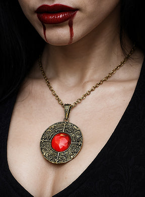 Eine Frau mit dunklem Haar trägt das „Magische Amulett mit rotem Edelstein Vampir“, ergänzt durch roten Lippenstift und Make-up, das an Blut erinnert, das aus ihrem Mund tropft.