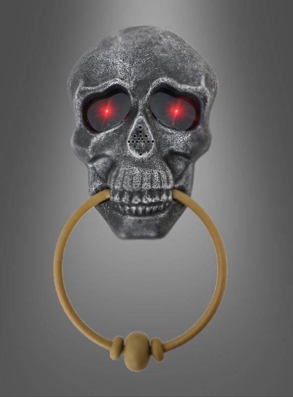 Wir präsentieren den Totenkopf-Türklopfer mit Licht und Sound: Ein metallener Totenkopf-Türklopfer mit leuchtend roten Augen und einem goldenen Ring im Mund vor einem grauen Farbverlauf – ideal als gruselige Halloween-Dekoration für ein Spukschloss oder als auffälliger Halloween-Türklopfer, um Ihre Gäste gebührend zu begrüßen.