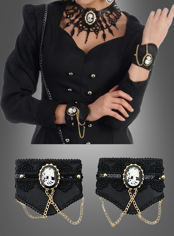 Eine Person, die ein schwarzes Kleid im viktorianischen Stil trägt, dazu ein schwarzes Spitzen-Cameo-Halsband, gotischen Armschmuck mit Brosche, Armfesseln mit Ketten, schwarze Manschetten sowie die unten abgebildeten passenden schwarzen Accessoires.