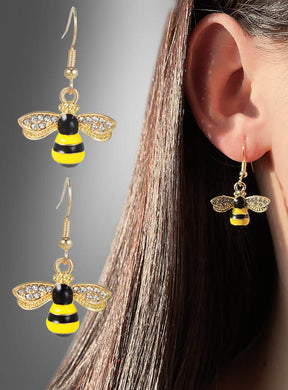 Nahaufnahme einer Person, die die „Bienen-Ohrringe mit Strass“ trägt – goldene Ohrringe in Bienenform, verziert mit gelben, schwarzen und Strass-Details –, ideal als „Bienen-Ohrringe“ oder als auffälliges Accessoire für ein Bienenkostüm; ein weiteres Paar dieser trendigen Modeschmuck-Ohrringe ist neben dem Ohr zu sehen.