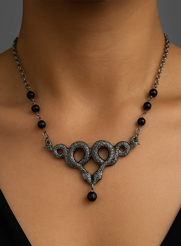 Die „Schlangenkette silber“ – eine silberne Halskette, verziert mit zwei ineinander verschlungenen Schlangenmotiven, schwarzen Perlen entlang der Kette und einem markanten schwarzen Anhänger in der Mitte – rundet jedes Kleopatra-Kostüm perfekt ab.
