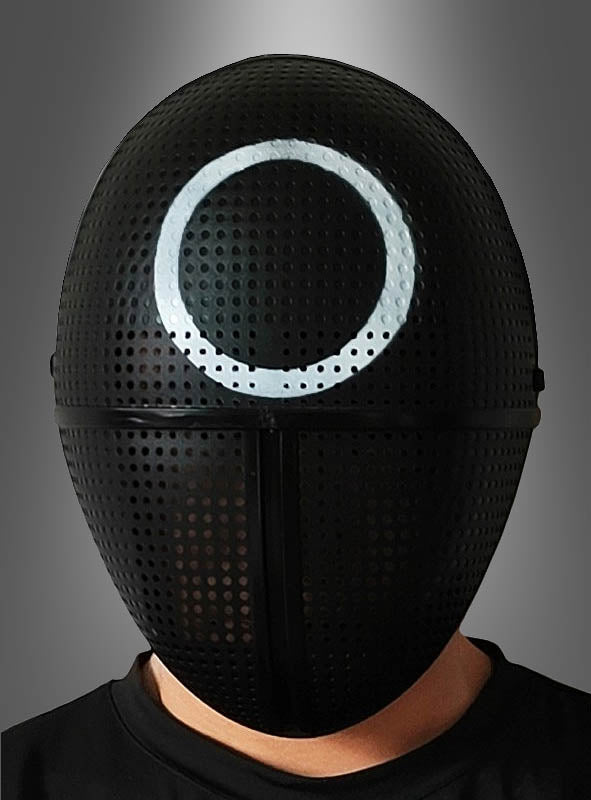 Eine Person, die die „Schwarze Maske mit Kreis für Game Cosplay“ trägt – eine schwarze, perforierte Maske mit einem weißen Kreis auf der Stirn, die an die Masken aus „Squid Game“ erinnert –, steht vor einem grau verlaufenden Hintergrund.
