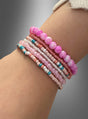 Ein Handgelenk, geschmückt mit dem „Hippie Perlen Armband Set rosa“ – sechs Perlenarmbänder in harmonischen Rosa-, Pfirsich-, Türkis- und Weißtönen – hebt sich deutlich von einem grauen Farbverlaufshintergrund ab. Jedes Armband strahlt den ungezwungenen Charme von Hippie-Schmuck aus und fängt die freigeistige Schönheit des Boho-Armband-Stils ein.