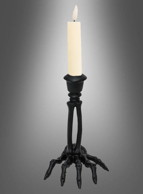 Der Kerzenständer „Skeletthand“ aus Kunstharz, schwarz, 16 cm, hält eine brennende weiße Kerze vor einem grauen Hintergrund mit Farbverlauf. Diese auffällige Halloween-Tischdekoration sorgt für eine gespenstische Atmosphäre und eignet sich daher ideal für gruselige Feiern.