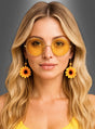 Eine Frau mit langen blonden Haaren trägt eine runde gelbe Sonnenbrille und dazu passende Sonnenblumen-Ohrringe für Hippies und blickt vor einem grauen Hintergrund direkt in die Kamera – ein perfektes Accessoire für jedes Karnevals-Outfit oder Hippie-Kostüm.