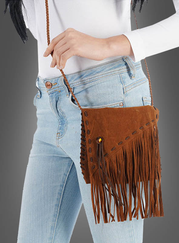 Eine Frau in hellblauen Jeans und einem weißen Oberteil hält die „Indianer Boho Tasche mit Fransen“ – eine stylische Fransentasche mit geflochtenem Riemen – vor einem grauen Hintergrund in der Hand.
