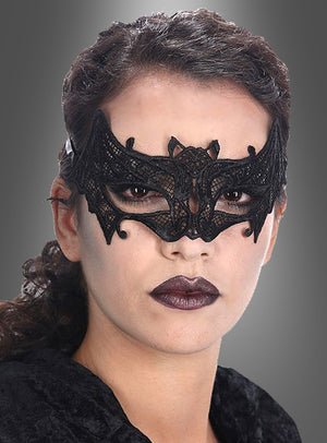 Eine Person mit dunklem Lippenstift, die eine Fledermaus-Augenmaske aus Spitze trägt, die an ein Gothic-Kostüm erinnert, vor einem grauen Hintergrund mit Farbverlauf.