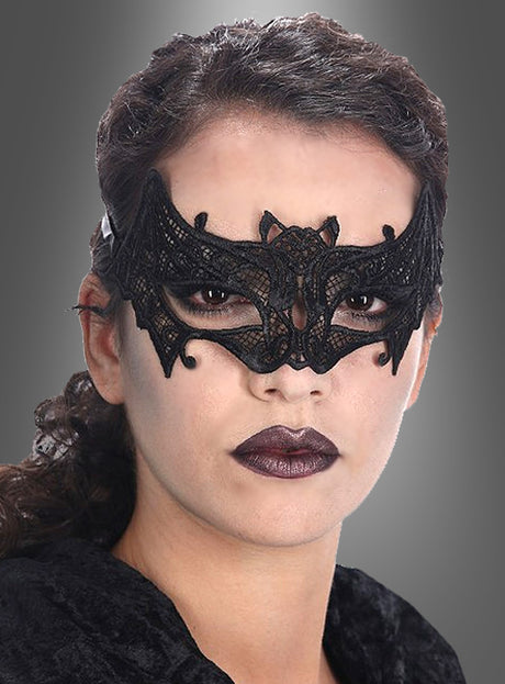 Eine Person mit dunklem Lippenstift, die eine Fledermaus-Augenmaske aus Spitze trägt, die an ein Gothic-Kostüm erinnert, vor einem grauen Hintergrund mit Farbverlauf.