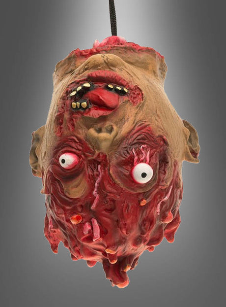 Eine bis ins grausame Detail ausgearbeitete Latex-Requisite in Form eines abgetrennten Zombie-Kopfes mit hervorquellenden Augen, freiliegenden Zähnen und blutigem, verwesendem Fleisch hängt kopfüber vor einem grauen Hintergrund mit Farbverlauf – perfekt für Ihre Halloween-Dekoration.