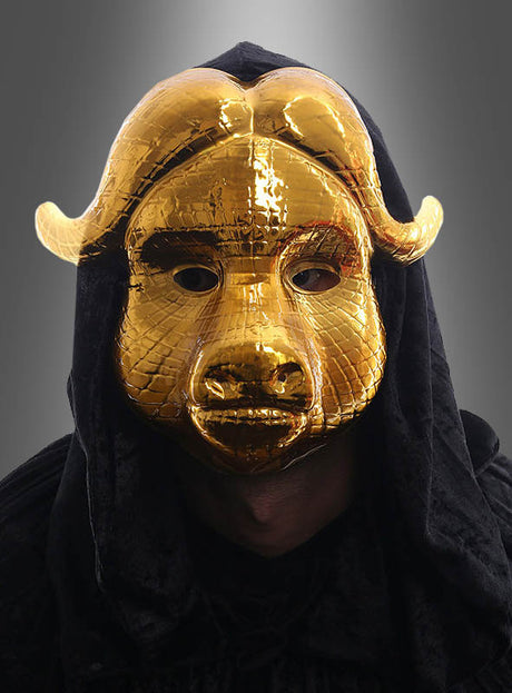 Eine Person, die die „Squad VIP Gast goldene Maske Stier“ trägt – eine glänzende, stierförmige goldene Maske mit markanten Hörnern – sowie einen schwarzen Kapuzenumhang, vor einem grauen Hintergrund mit Farbverlauf.