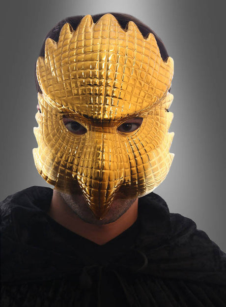 Eine Person trägt die „Squad Game VIP“-Maske „Goldene Adler“ – eine glänzende, goldene, vogelähnliche Maske mit aufwendigen Federmustern –, kombiniert mit einem dunklen Umhang und vor einem grauen Hintergrund mit Farbverlauf. Das markante Design spiegelt den geheimnisvollen Reiz der legendären „Squid Game VIP“-Maske wider.