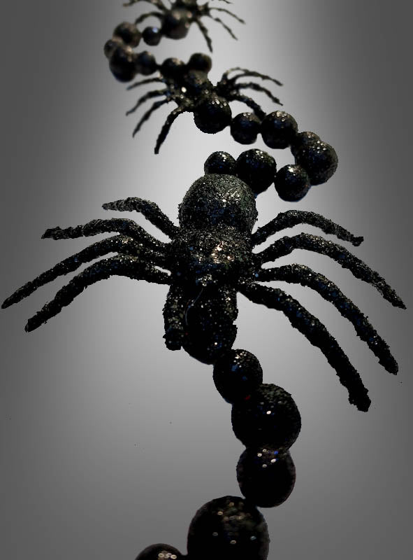 Nahaufnahme der „Schwarze Spinnen Girlande 160 cm“, einer schwarzen, glitzernden Halloween-Dekoration mit Plastikspinnen und Perlen, die in einer Reihe angeordnet sind und vor einem Hintergrund mit Farbverlauf präsentiert werden.