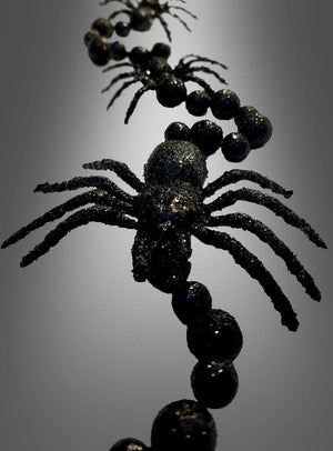 Nahaufnahme der „Schwarze Spinnen Girlande 160 cm“, einer schwarzen, glitzernden Halloween-Dekoration mit Plastikspinnen und Perlen, die in einer Reihe angeordnet sind und vor einem Hintergrund mit Farbverlauf präsentiert werden.