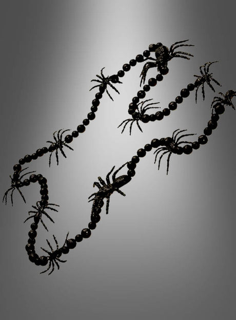 Eine schwarze Spinnengirlande (160 cm) mit schwarzen Perlen und mehreren schwarzen Plastikspinnen, ideal als Spinnendekoration oder Halloween-Dekoration, vor einem grauen Hintergrund mit Farbverlauf.