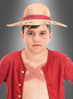 Ein Junge mit Strohhut, rotem, offenem Hemd und einer Narbe auf der Brust, verkleidet als Strohhut-Ruffy aus „One Piece“, steht vor einem grauen Hintergrund – die perfekte Inspiration für einen „One Piece“-Kindergeburtstag oder alle, die auf der Suche nach einzigartigen „One Piece“-Papierkopfbedeckungen sind.