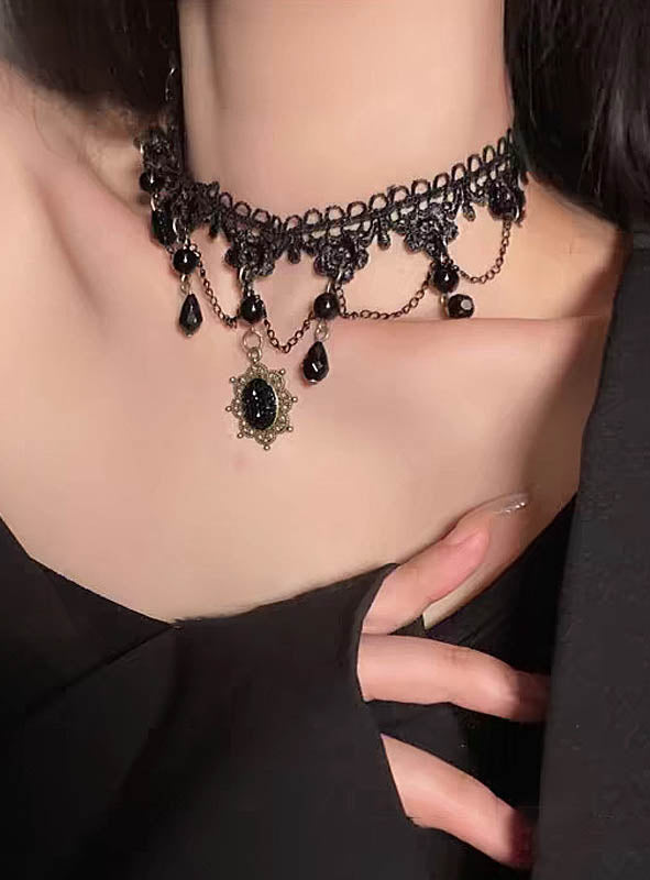 In einem schwarzen, schulterfreien Outfit präsentiert eine Person elegant die „Gothic Collier Halskette schwarz“ – ein schwarzes Spitzen-Choker-Halsband, verziert mit herabhängenden schwarzen Perlen und einem kunstvoll gearbeiteten schwarzen Anhänger. Mit seiner schwarzen Spitze verkörpert dieses atemberaubende Schmuckstück den Inbegriff von Vampir-Schmuck und verleiht dem Gesamtlook einen Hauch von gotischer Raffinesse.