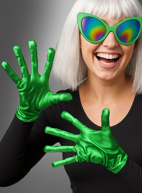 Eine Person mit weißem Haar trägt eine Regenbogen-Cat-Eye-Sonnenbrille, ein schwarzes Shirt und „Grüne Alien-Handschuhe“ mit glänzenden, länglichen Fingern – ein außerirdisches Alien-Kostüm-Accessoire –, während sie lächelnd und verspielt vor einem grauen Hintergrund posiert.